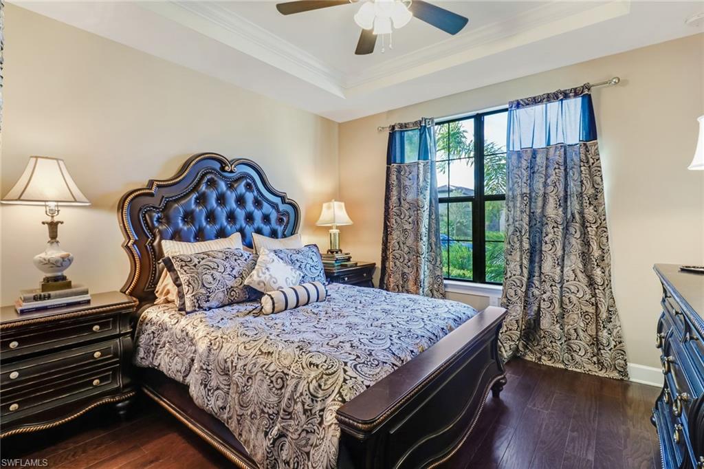 Bedroom with ornamental molding, a tray ceiling, dark wood-style floors, and a ceiling fan