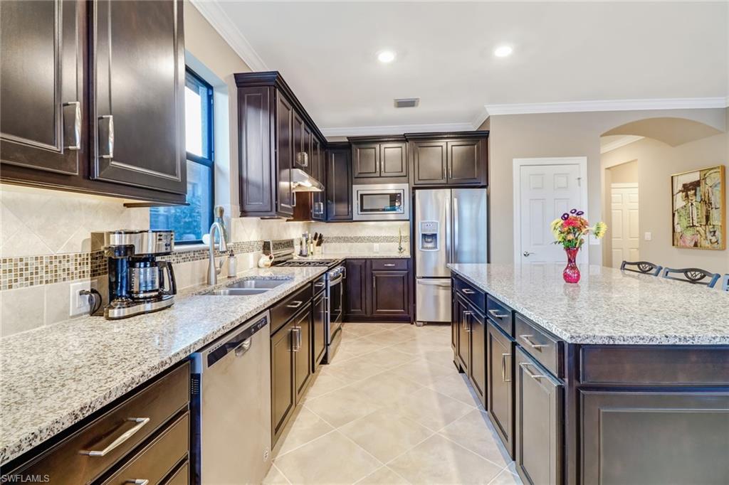 Kitchen with dark brown cabinetry, ornamental molding, light stone counters, appliances with stainless steel finishes, and recessed lighting