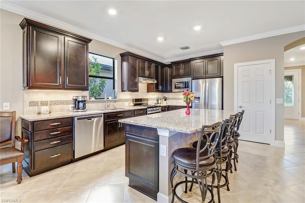 Kitchen featuring tasteful backsplash, dark brown cabinetry, ornamental molding, stainless steel appliances, and light stone countertops