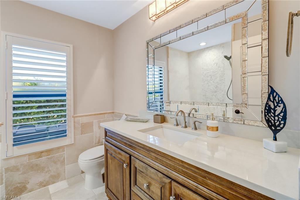 Bathroom featuring tile walls, vanity, a shower, light tile patterned floors, and a wainscoted wall
