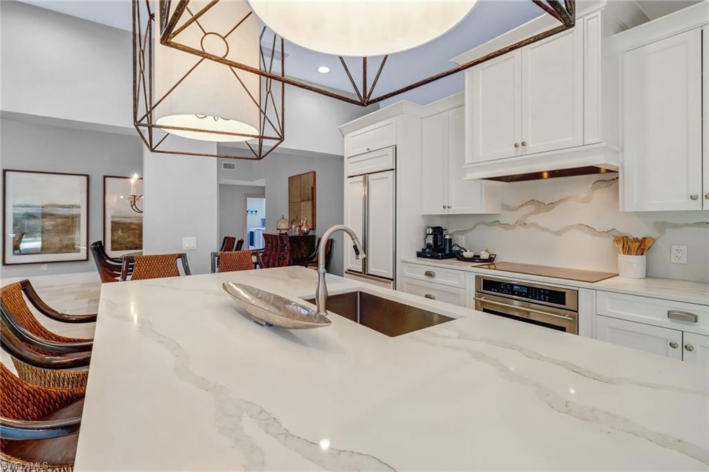 Kitchen with light stone countertops, white cabinets, oven, hanging light fixtures, and recessed lighting