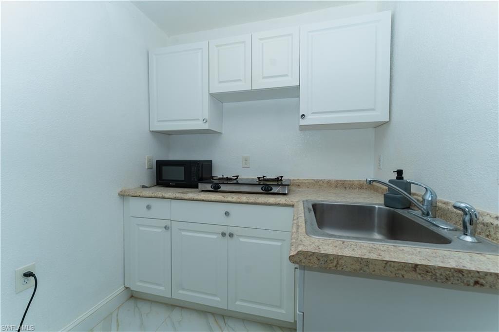 Kitchen featuring white cabinetry, light marble finish floors, black microwave, and light countertops