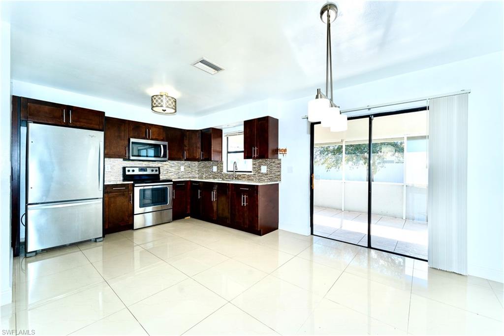 Kitchen featuring stainless steel appliances, dark brown cabinetry, backsplash, decorative light fixtures, and light tile patterned flooring