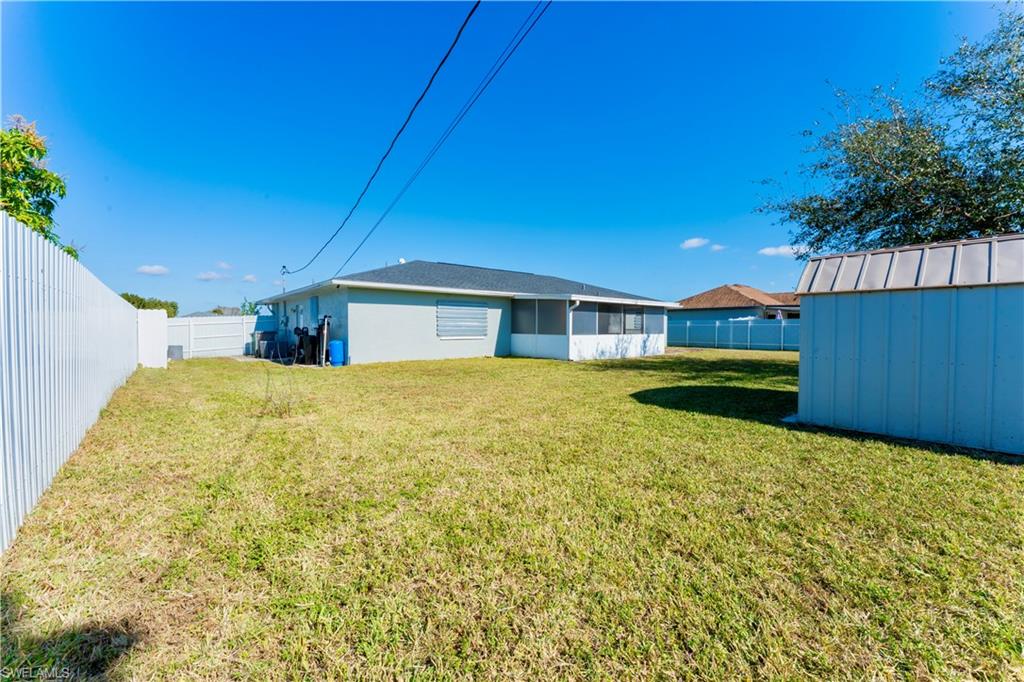 Rear view of house with a fenced backyard and a storage unit