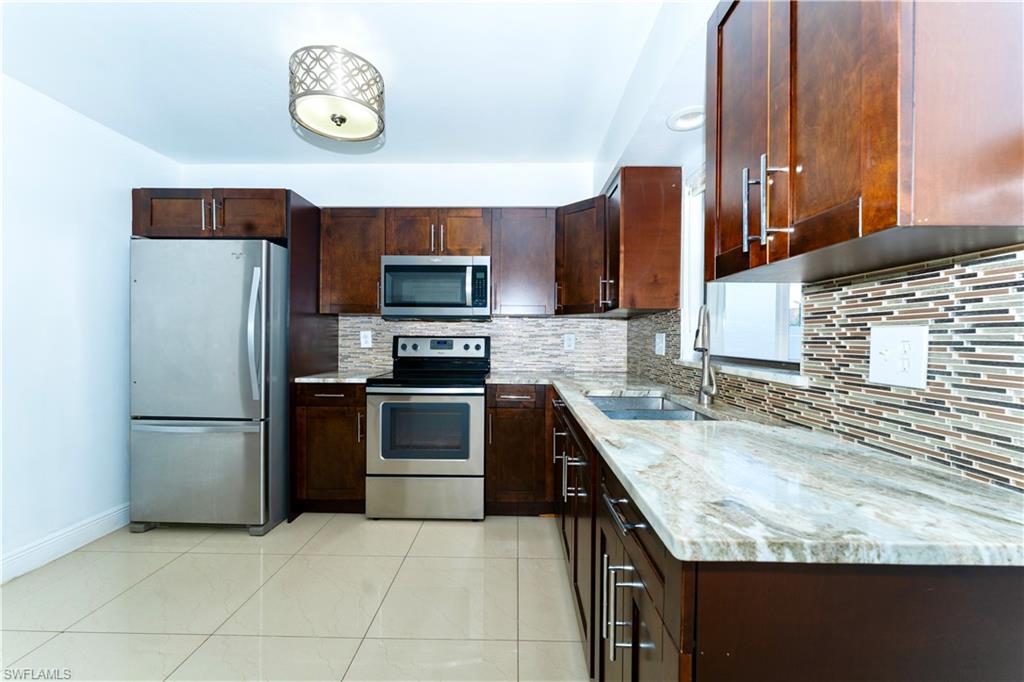 Kitchen featuring appliances with stainless steel finishes, light stone countertops, backsplash, and dark brown cabinetry