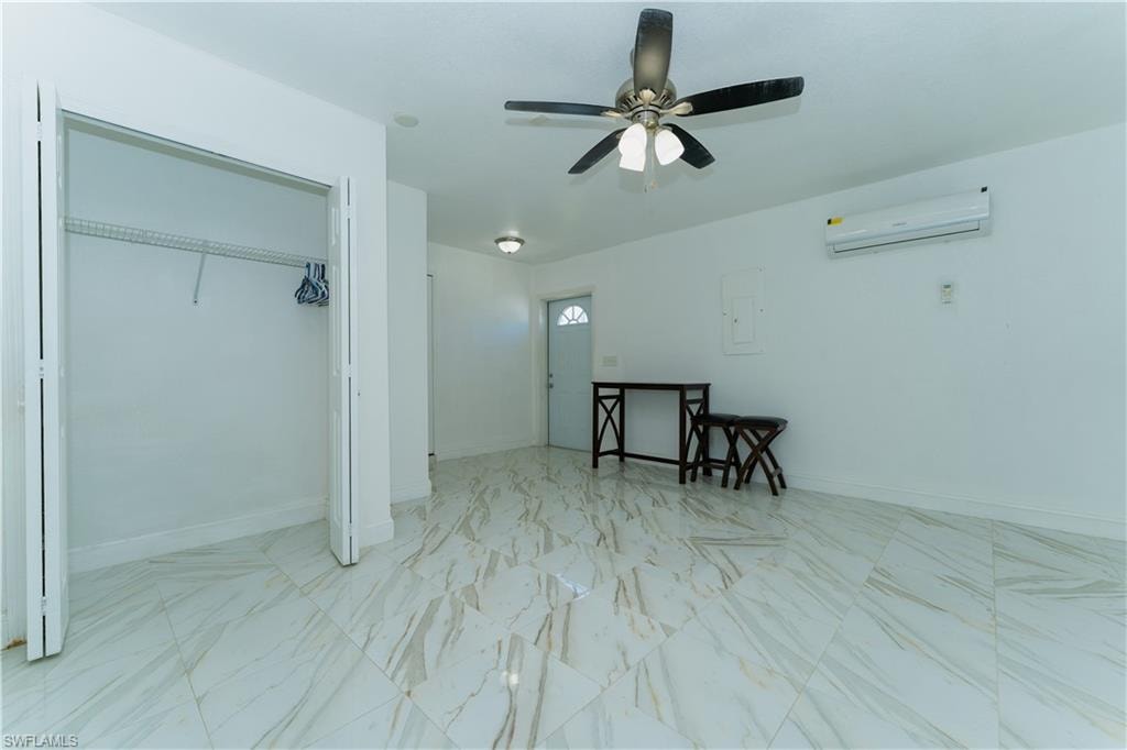 Bedroom with light marble finish floors, a closet, a wall unit AC, ceiling fan, and electric panel