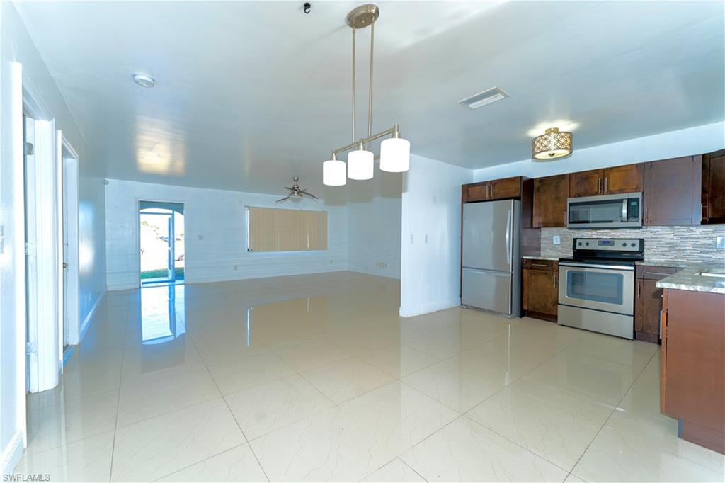 Kitchen featuring appliances with stainless steel finishes, hanging light fixtures, a ceiling fan, light stone counters, and backsplash