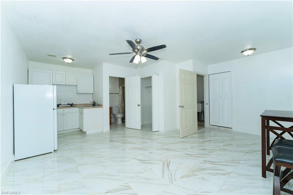 Kitchen featuring freestanding refrigerator, light marble finish floors, a ceiling fan, and white cabinets