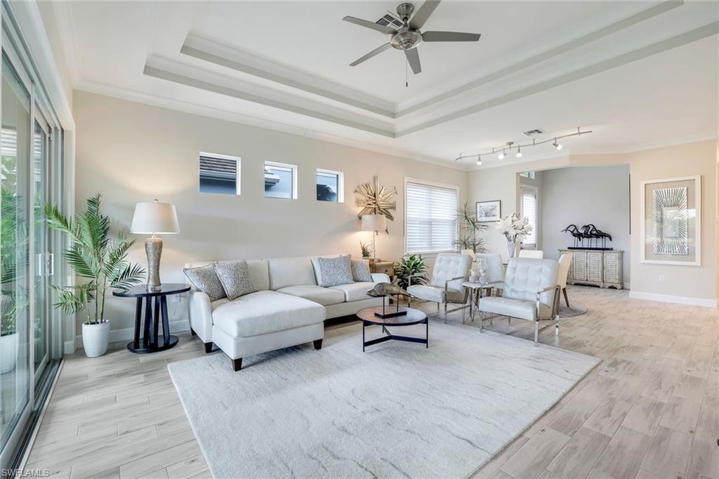 Living room with a raised ceiling, crown molding, light hardwood / wood-style flooring, and ceiling fan