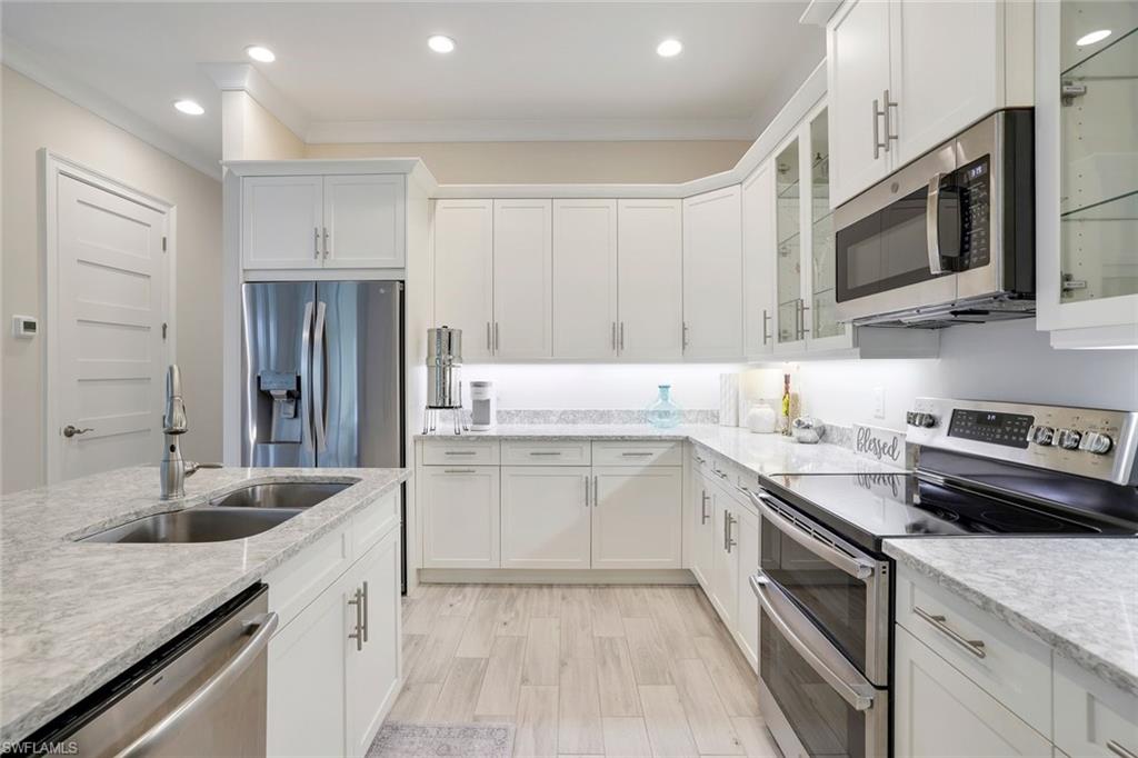 Kitchen with light stone countertops, appliances with stainless steel finishes, sink, white cabinets, and light hardwood / wood-style floors