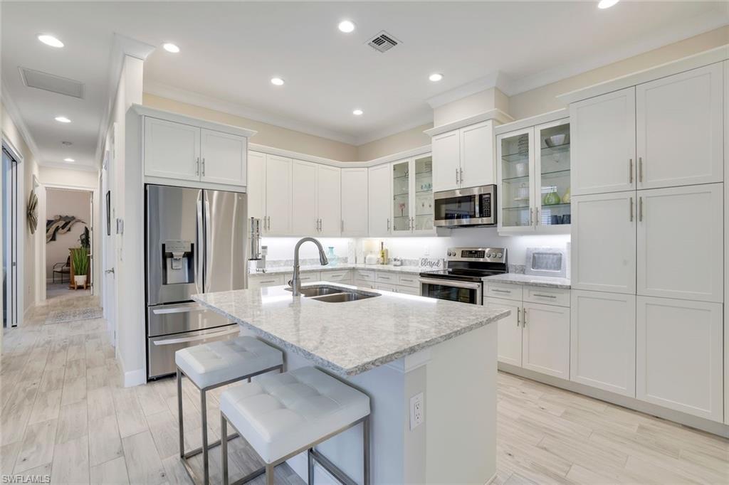 Kitchen featuring sink, stainless steel appliances, light stone counters, a center island with sink, and light wood-type flooring