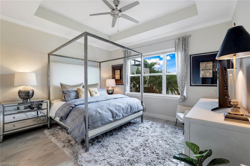 Bedroom with a raised ceiling, ceiling fan, wood-type flooring, and ornamental molding