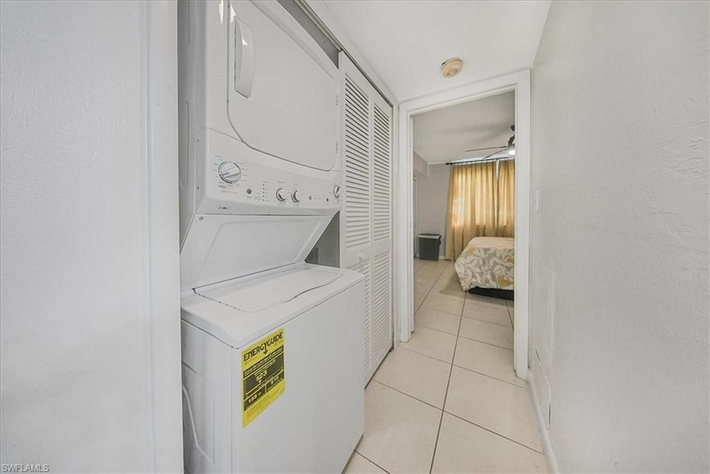 Laundry area featuring stacked washing machine and dryer, light tile patterned flooring, a textured wall, and a ceiling fan