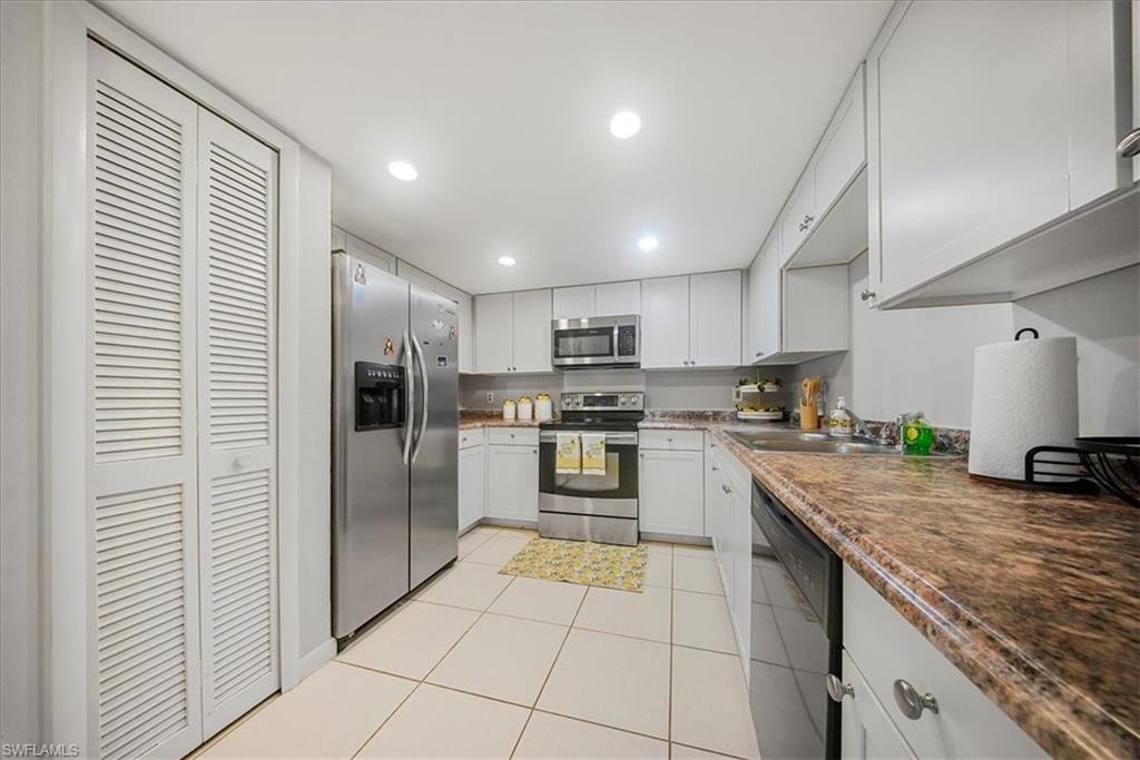 Kitchen with appliances with stainless steel finishes, light tile patterned floors, white cabinetry, recessed lighting, and dark countertops