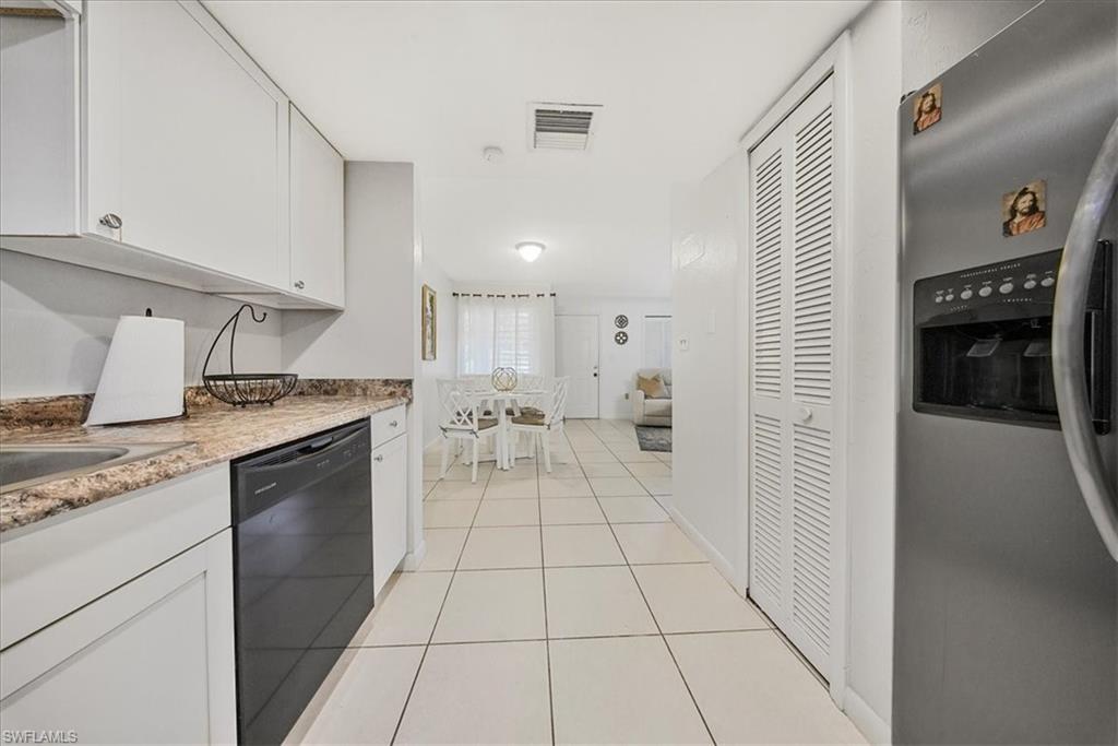 Kitchen with stainless steel fridge with ice dispenser, white cabinetry, light tile patterned flooring, black dishwasher, and light stone counters