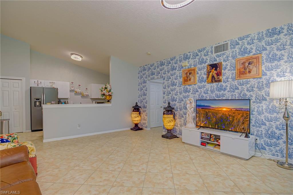 Living area featuring vaulted ceiling, wallpapered walls, and light tile patterned floors