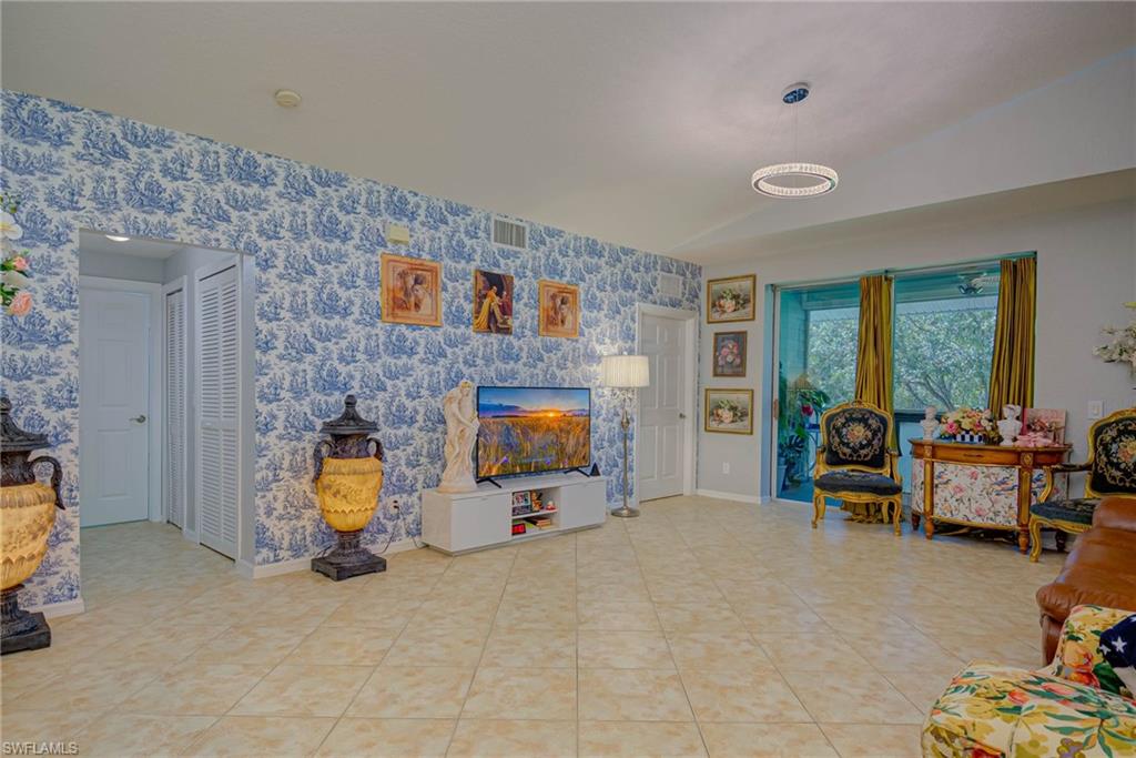 Living area featuring wallpapered walls, vaulted ceiling, and light tile patterned floors