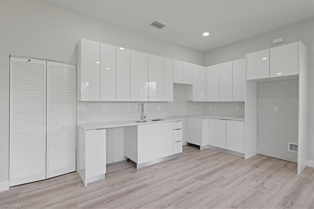 Kitchen with modern cabinets, white cabinetry, decorative backsplash, light wood finished floors, and recessed lighting