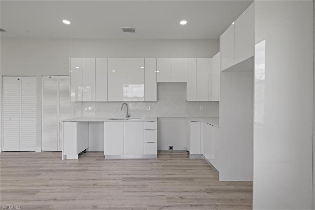 Kitchen with white cabinets, modern cabinets, light wood-style floors, decorative backsplash, and recessed lighting