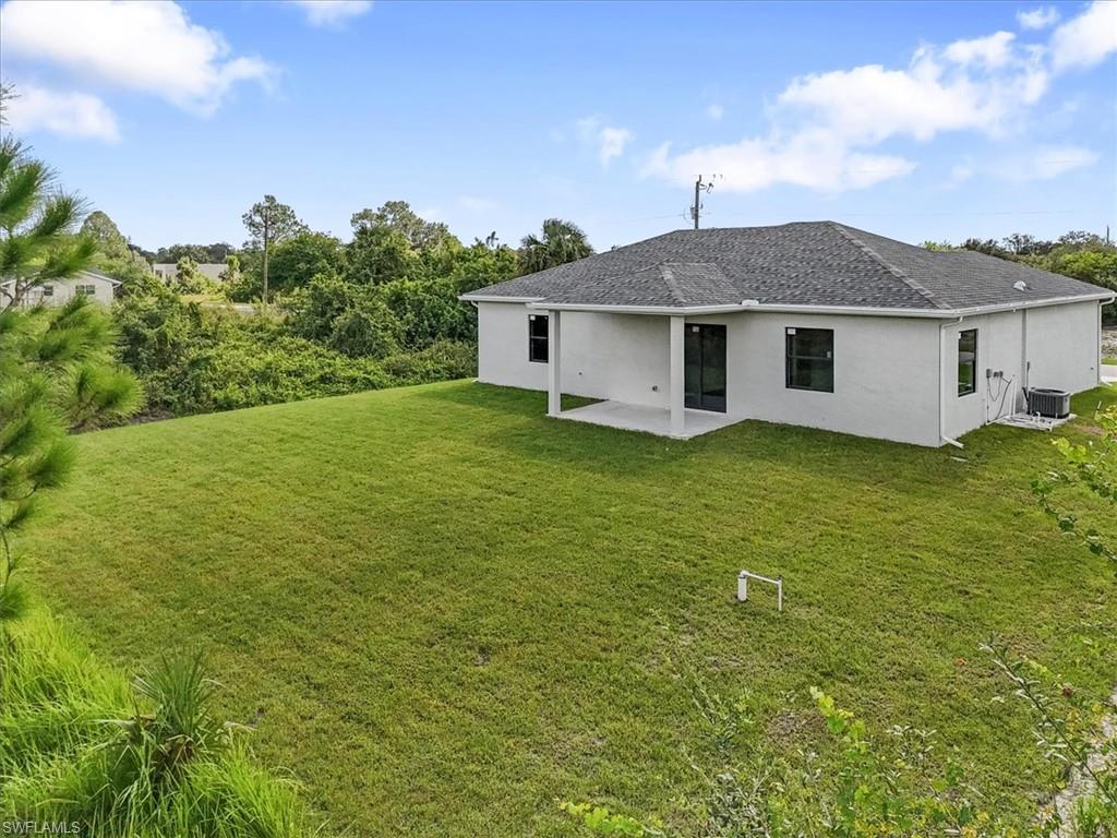 Rear view of property featuring a patio area, stucco siding, a lawn, and roof with shingles