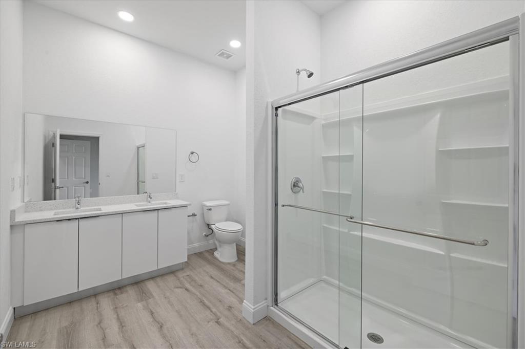 Full bath with double vanity, light wood-style floors, a stall shower, and recessed lighting