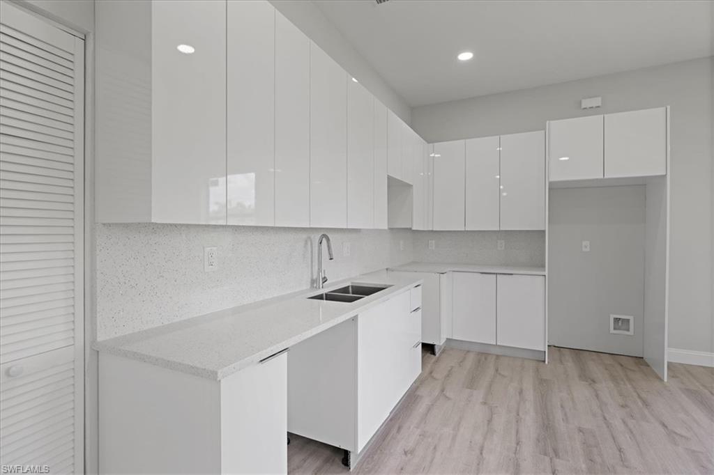 Kitchen featuring modern cabinets, white cabinets, backsplash, light stone counters, and light wood finished floors