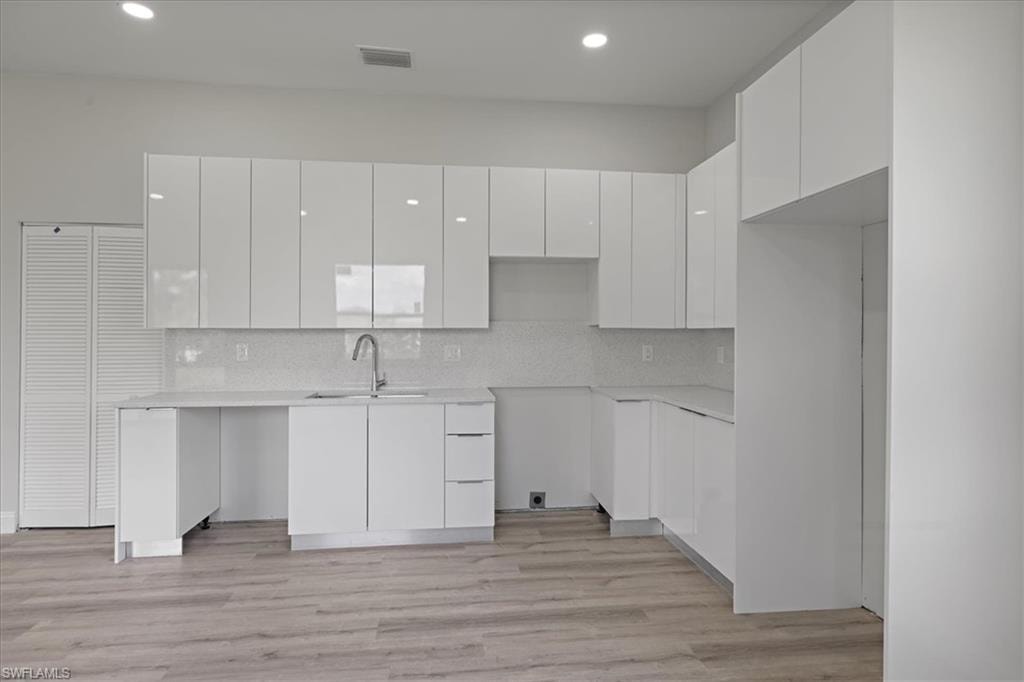 Kitchen featuring modern cabinets, white cabinets, light wood finished floors, tasteful backsplash, and recessed lighting