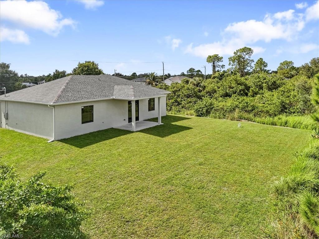 Rear view of property featuring a patio, a lawn, a shingled roof, and stucco siding