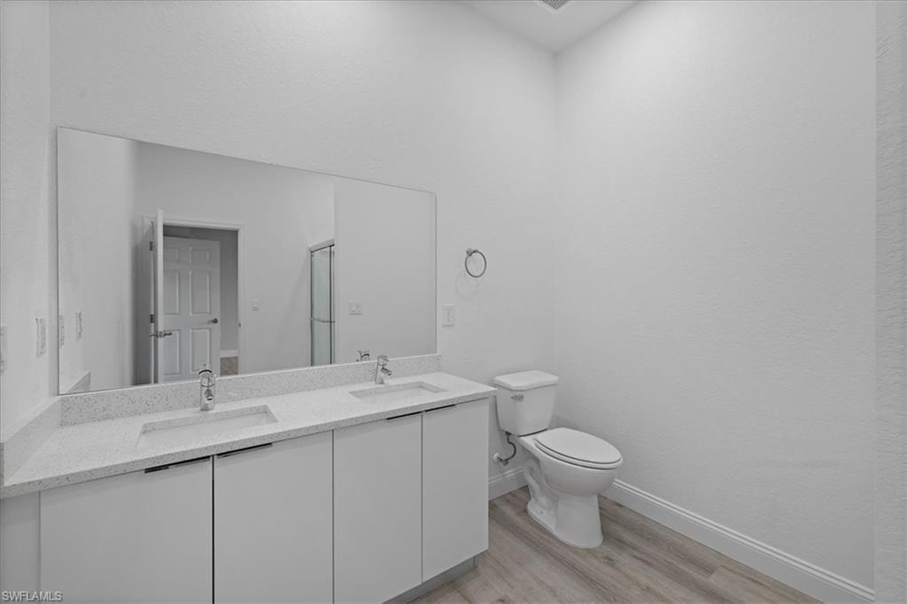 Bathroom featuring light wood-style floors, double vanity, and a stall shower