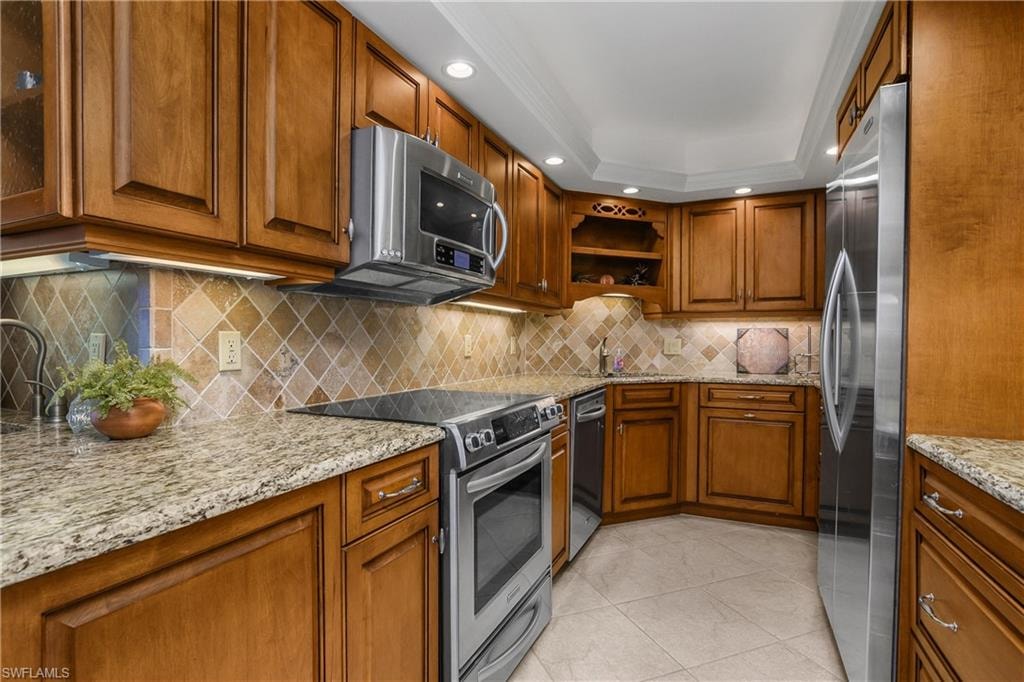 Kitchen featuring brown cabinetry, appliances with stainless steel finishes, light tile patterned floors, light stone counters, and open shelves
