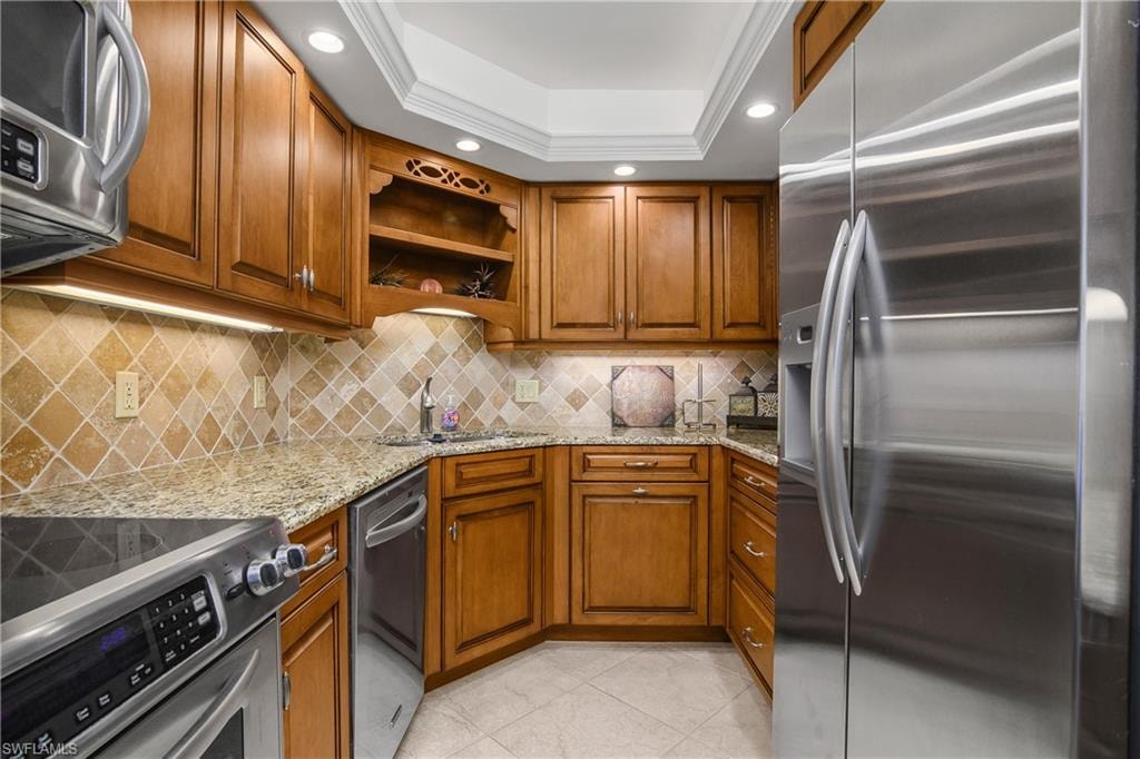 Kitchen with appliances with stainless steel finishes, brown cabinets, light stone counters, and recessed lighting