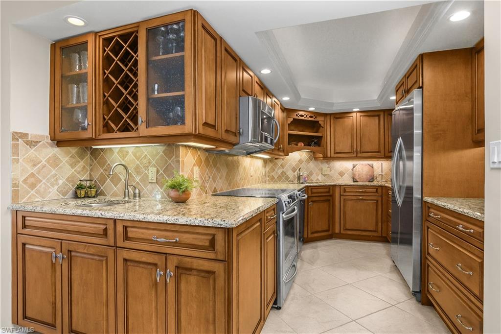 Kitchen with, wet bar, stainless steel appliances, light stone counters, light tile patterned floors, and glass insert cabinets
