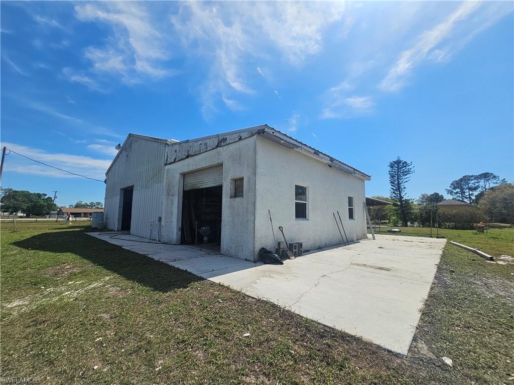 View of side of property with driveway, a garage, an outbuilding, a yard, and stucco siding