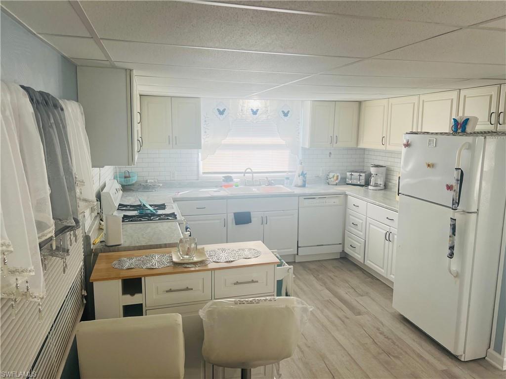 Kitchen with white appliances, white cabinets, light wood finished floors, light countertops, and a paneled ceiling