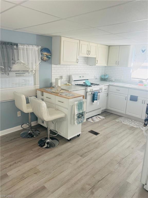Kitchen with light countertops, white range with gas cooktop, white cabinetry, light wood-style flooring, and backsplash