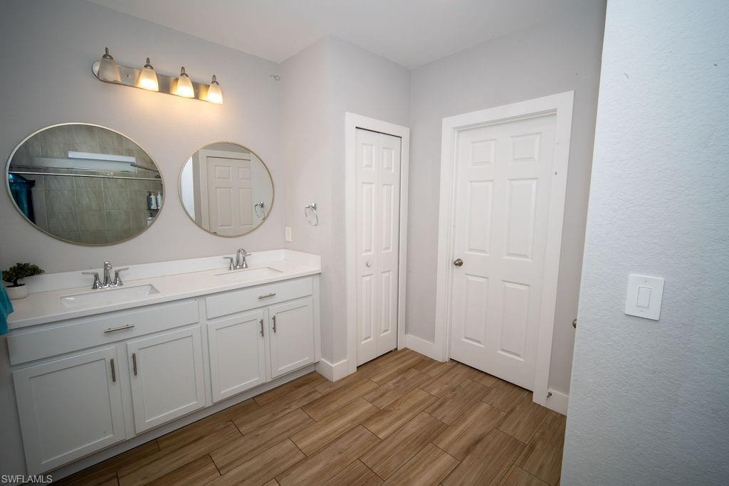 Full bath featuring double vanity, light wood-style floors, and tiled shower