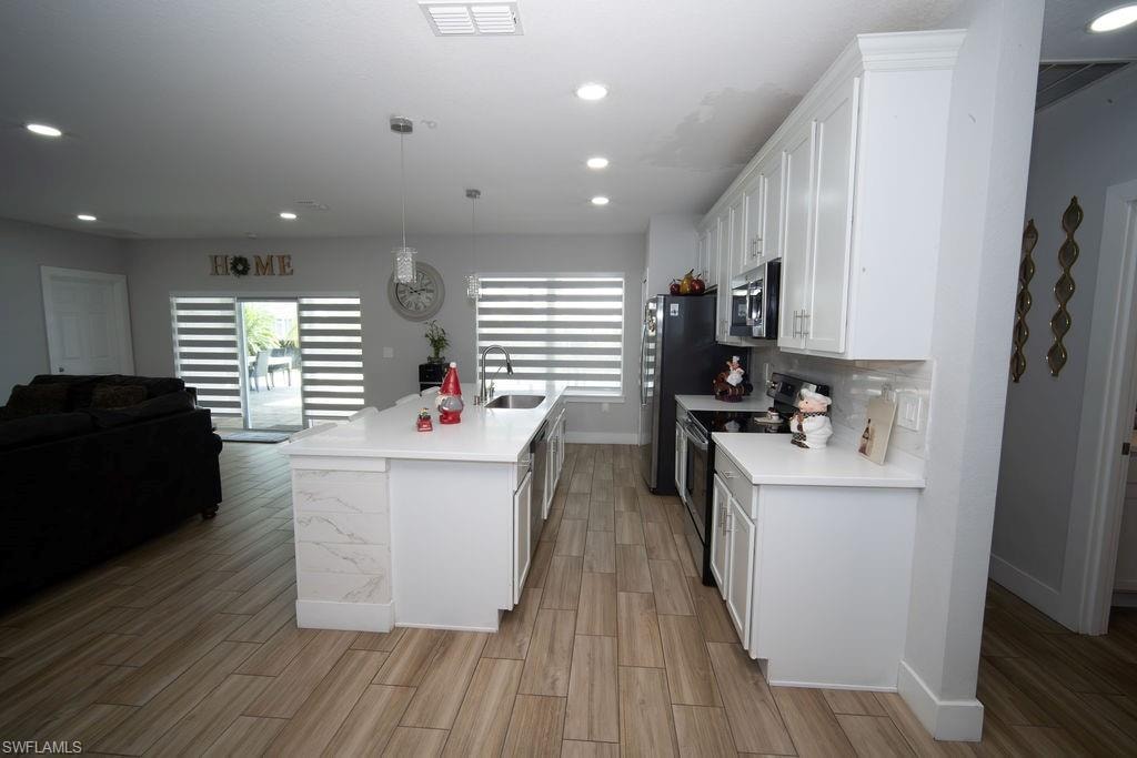 Kitchen with white cabinetry, appliances with stainless steel finishes, open floor plan, pendant lighting, and an island with sink