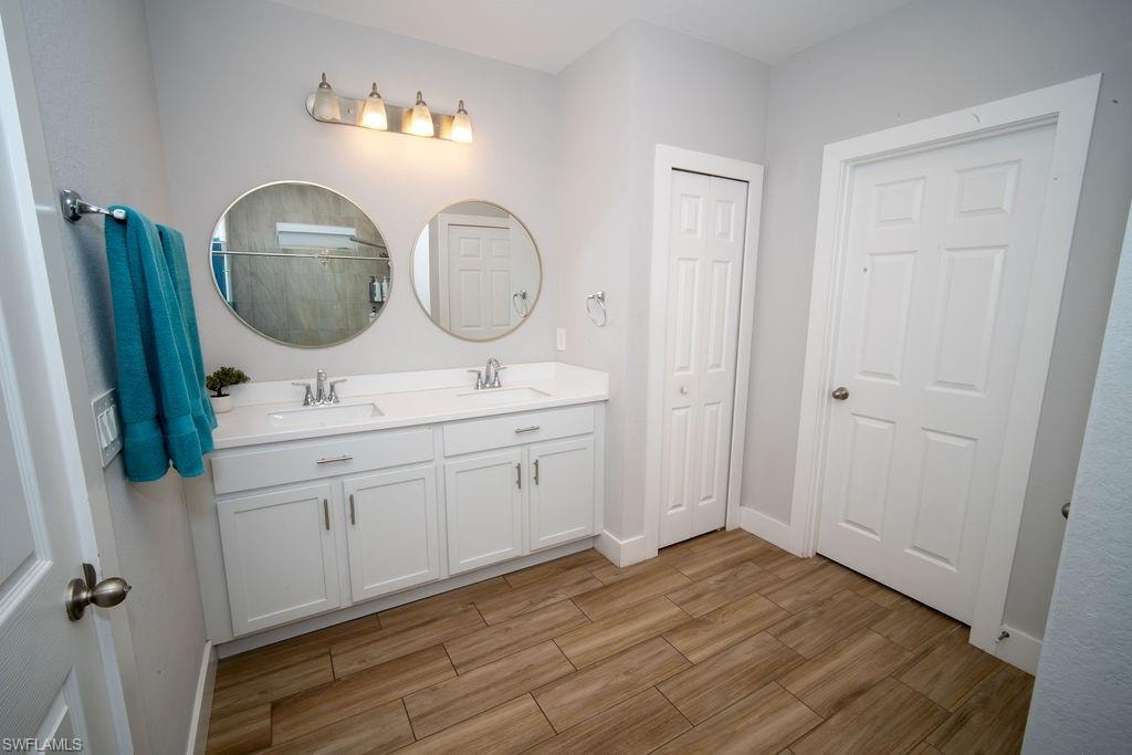 Full bath with double vanity, light wood-type flooring, and a stall shower