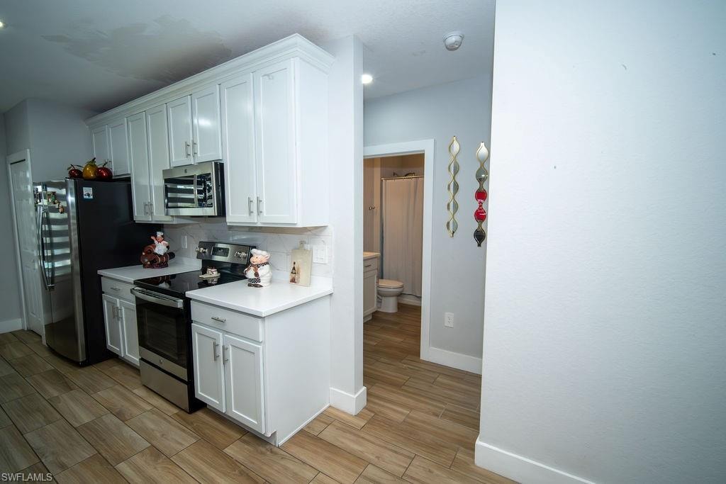 Kitchen with appliances with stainless steel finishes, light countertops, wood finish floors, decorative backsplash, and white cabinets