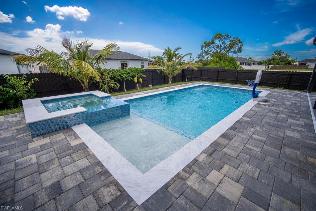 View of pool featuring a pool with connected hot tub, a fenced backyard, and a patio area