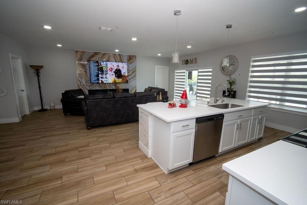 Kitchen with white cabinets, wood tiled floors, open floor plan, stainless steel dishwasher, and recessed lighting