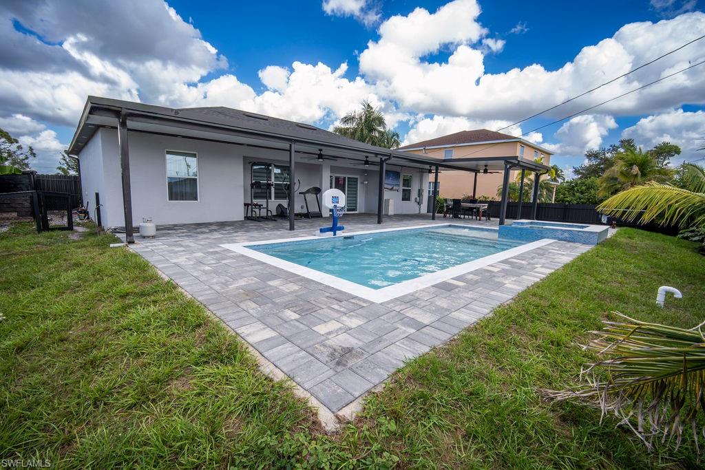 Rear view of house with a fenced backyard, a ceiling fan, a patio, and a pool with connected hot tub