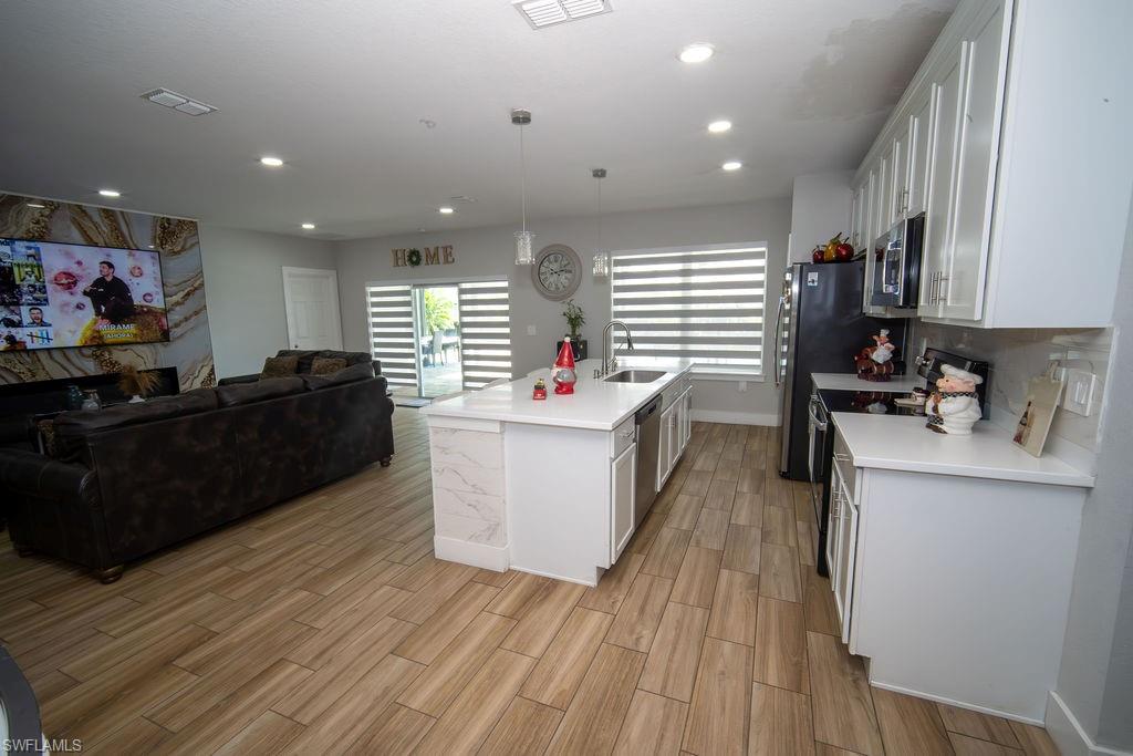 Kitchen with open floor plan, white cabinets, appliances with stainless steel finishes, decorative light fixtures, and an island with sink