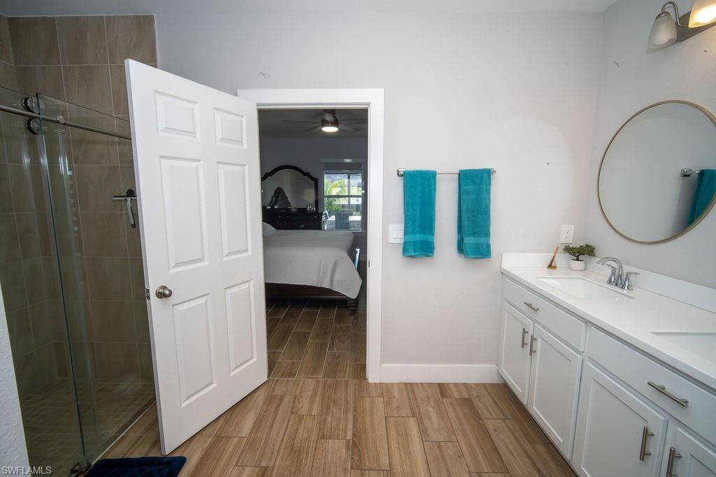 Bathroom with connected bathroom, wood tiled floors, double vanity, a shower stall, and ceiling fan