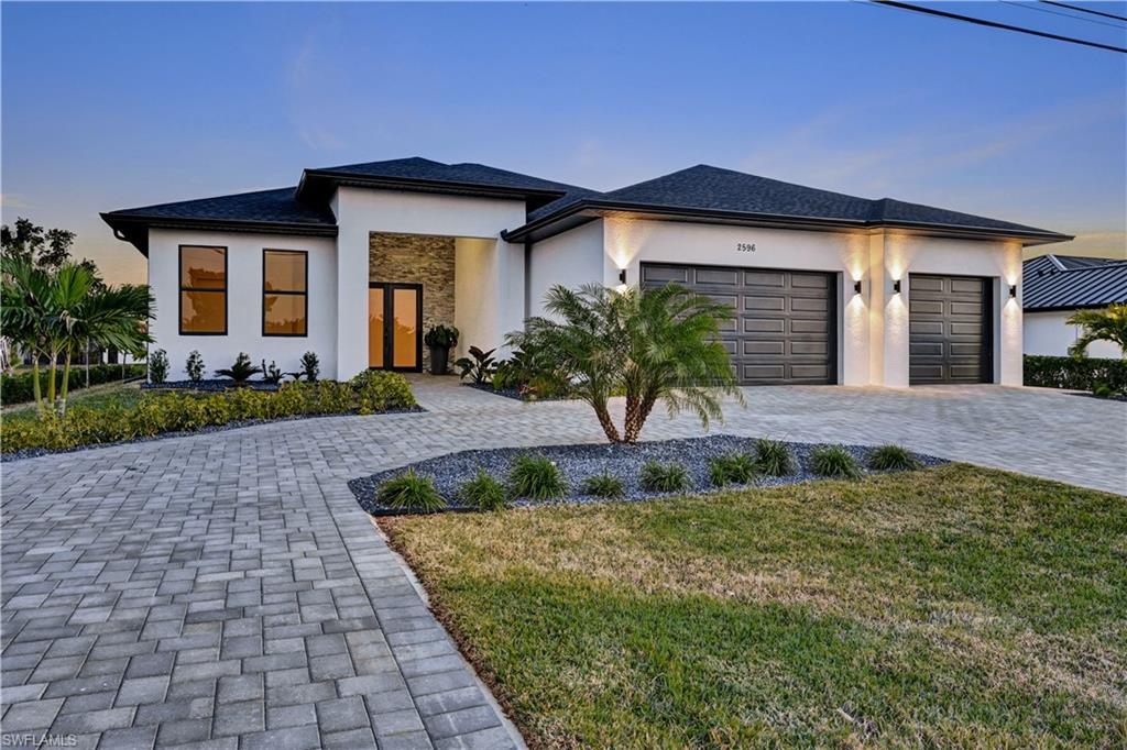 Prairie-style home with stucco siding, decorative driveway, a front yard, and an attached garage
