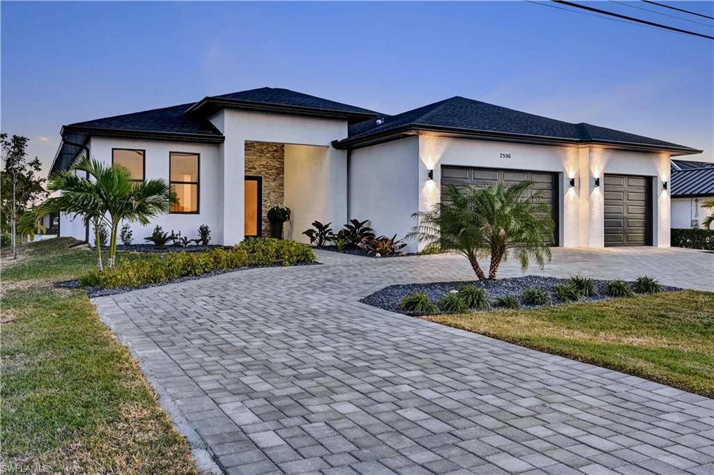 Prairie-style home featuring stucco siding, decorative driveway, an attached garage, and a front lawn
