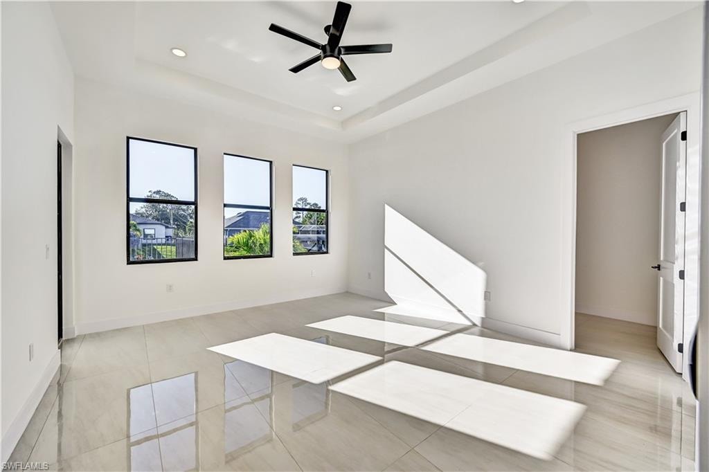 Unfurnished bedroom with a tray ceiling, a ceiling fan, recessed lighting, and light tile patterned flooring
