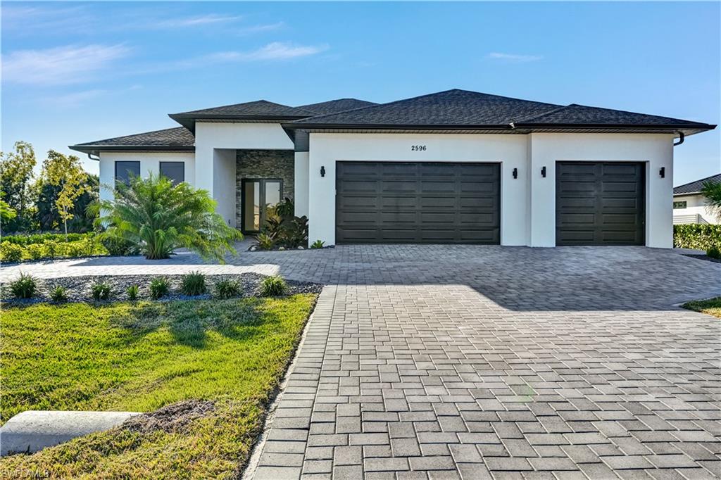 Prairie-style home with stucco siding, decorative driveway, an attached garage, and a front lawn