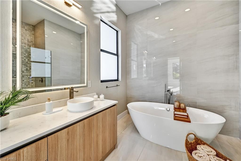 Bathroom with tile walls, vanity, a freestanding bath, and light tile patterned floors