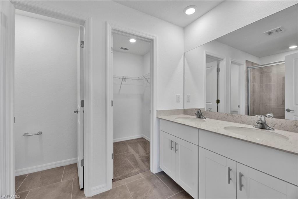 Full bathroom featuring double vanity, a spacious closet, light tile patterned flooring, a stall shower, and light carpet
